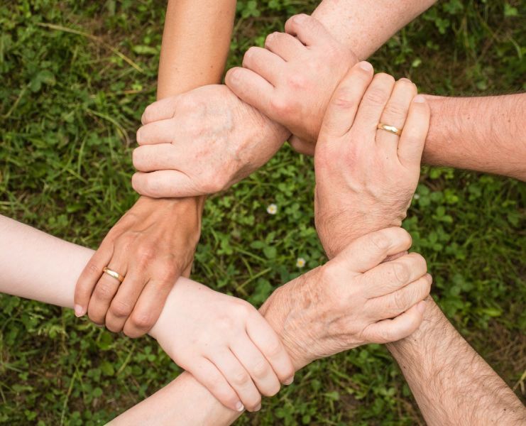 Sechs Hände fassen jeweils an das Handgelenk einer anderen Person und bilden dadurch einen Kreis.