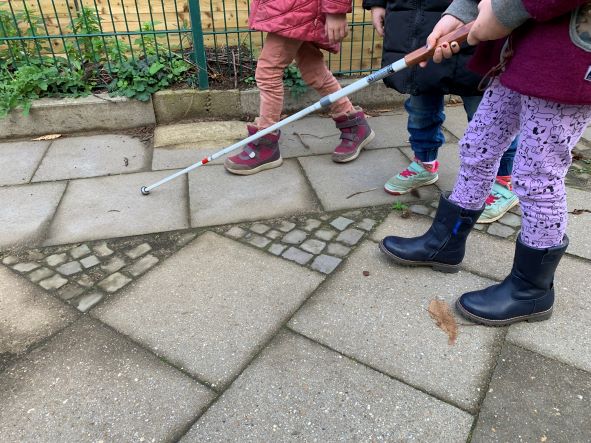 Drei Kinder, die einen Blindenstock benutzen